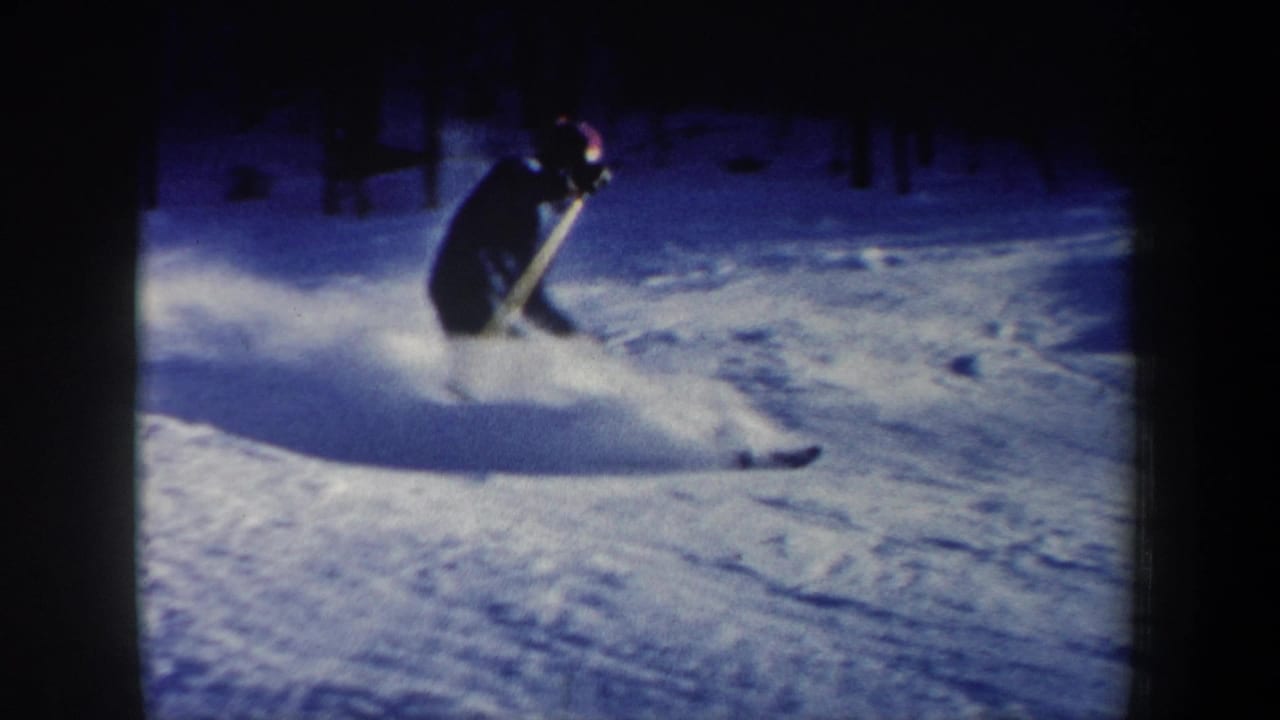 1962 New Hampshire 8mm frame showing a skier in dark winter clothing and red hat carving through powder on a snowy slope.