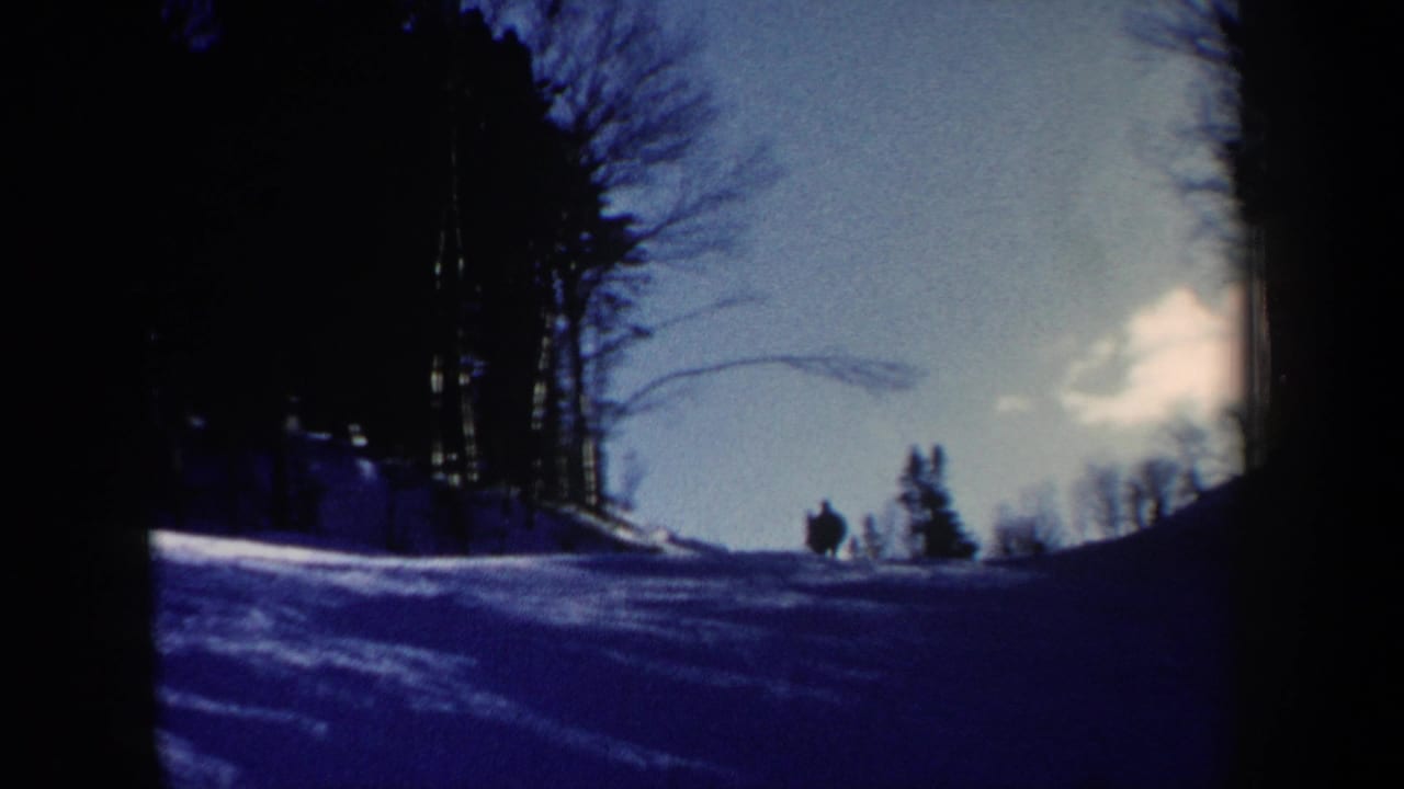 1962 New Hampshire 8mm frame looking across a snowy slope toward bare trees, with a small skier silhouette near the forest edge.