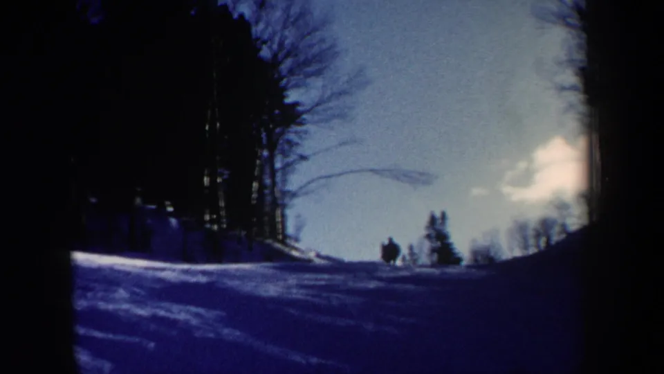 1962 New Hampshire 8mm frame looking across a snowy slope toward bare trees, with a small skier silhouette near the forest edge.