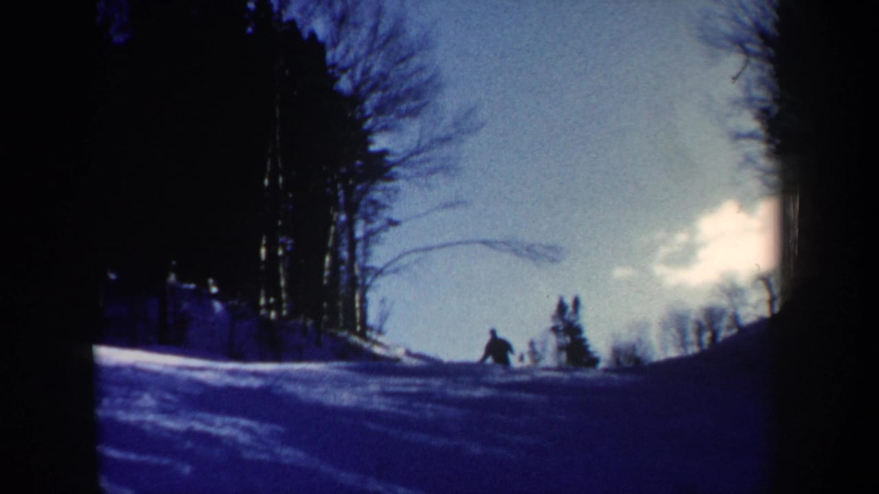 1962 New Hampshire 8mm frame showing a lone skier as a dark silhouette on a snow-covered slope with bare trees and bright sky.