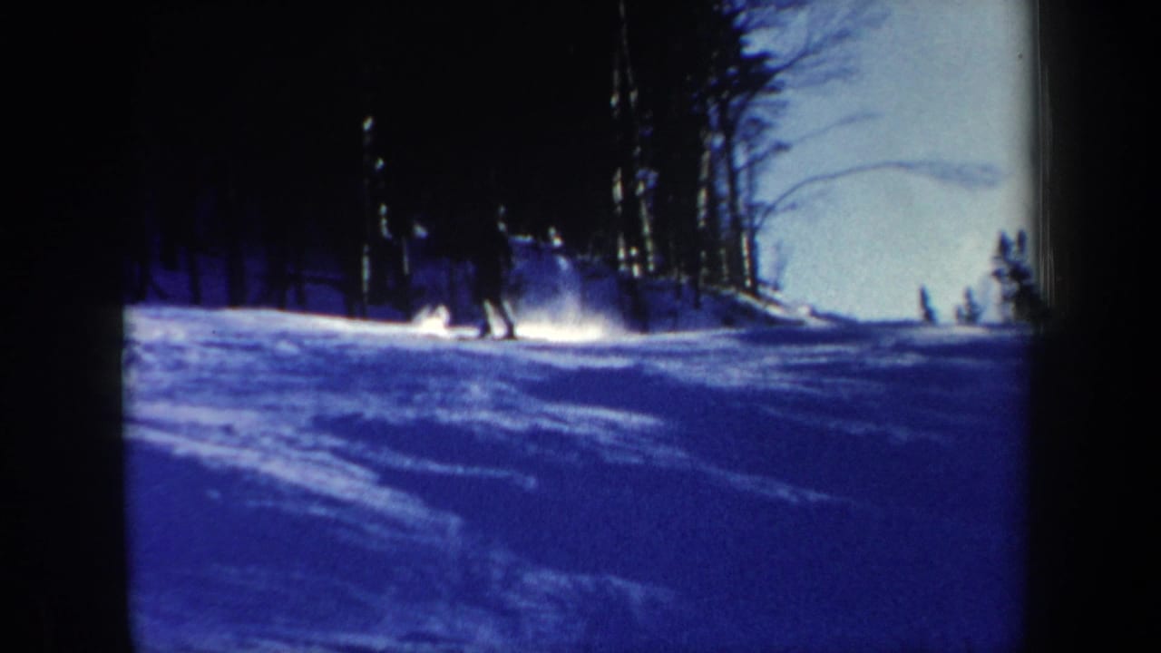 1962 New Hampshire home-movie frame showing small skiers on a snow-covered hillside under blue dusk light.