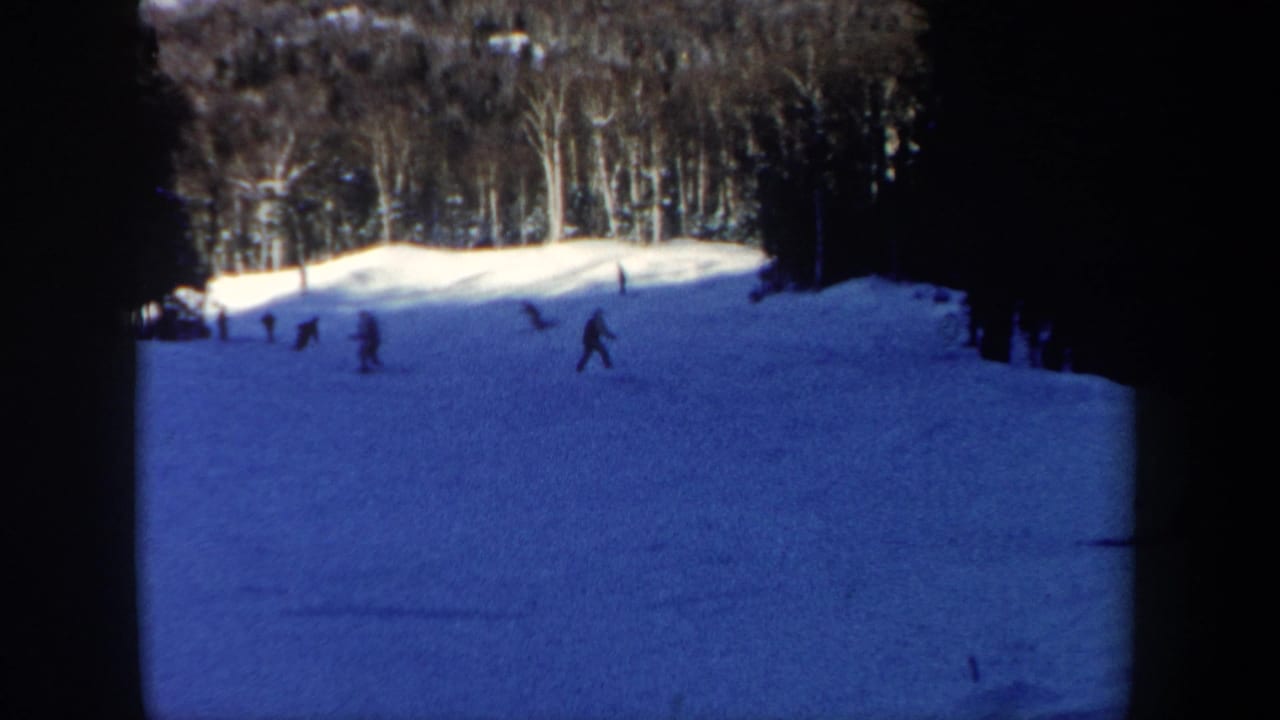 Distant skiers cross a snowy New Hampshire hillside in a soft, blue-tinted 1962 8mm home-movie frame.