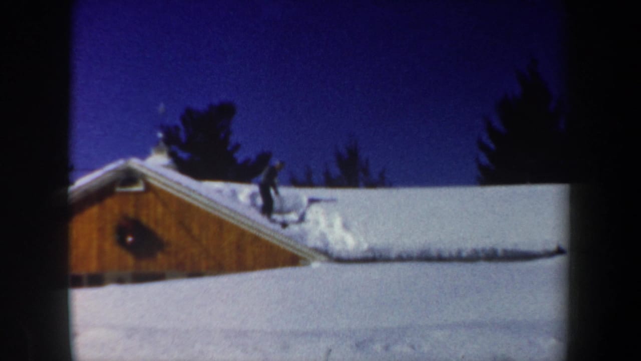 A rooftop figure appears to work in snow on a wooden building in this 1962 New Hampshire winter home-movie frame.