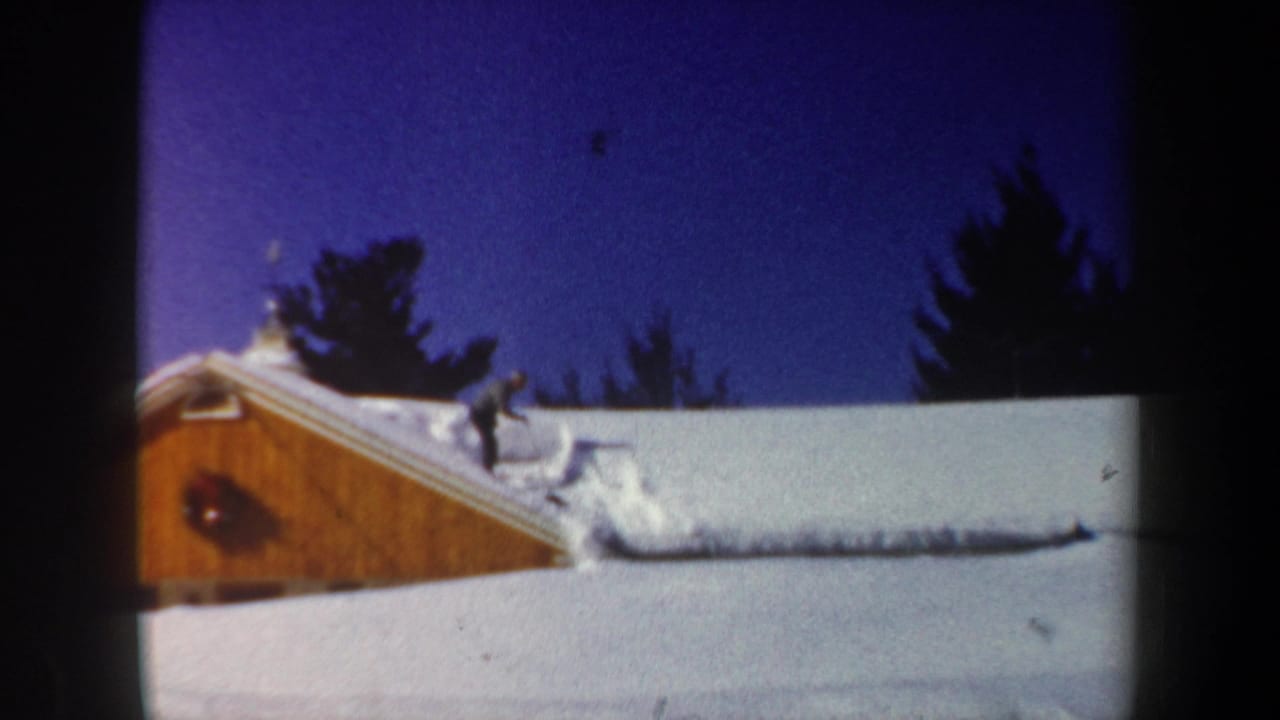 Snowy cabin roof with a person shoveling near the ridge.