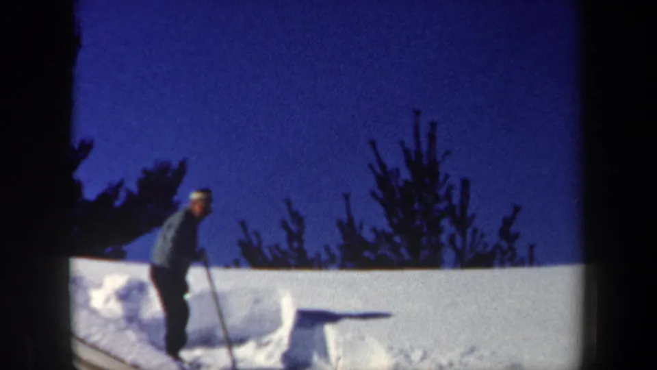 A bundled person holding a shovel stands on the snowy cabin roof in this 1962 New Hampshire winter frame.
