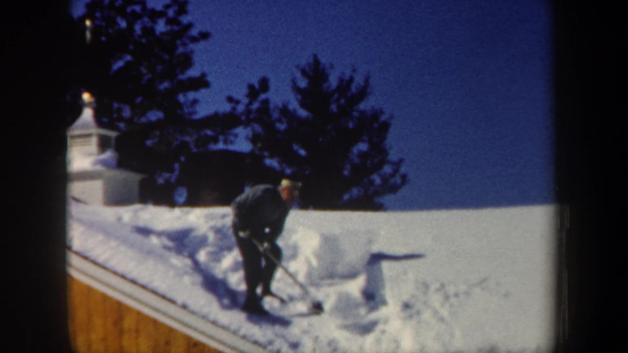 The man pauses upright with his shovel while clearing snow from a New Hampshire roof in 1962.