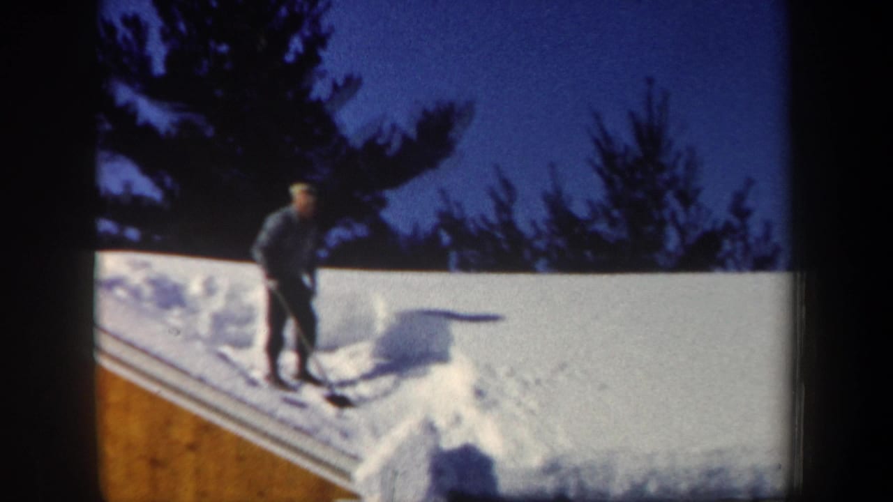 Man standing on a snow-covered roof under a dark blue winter sky.