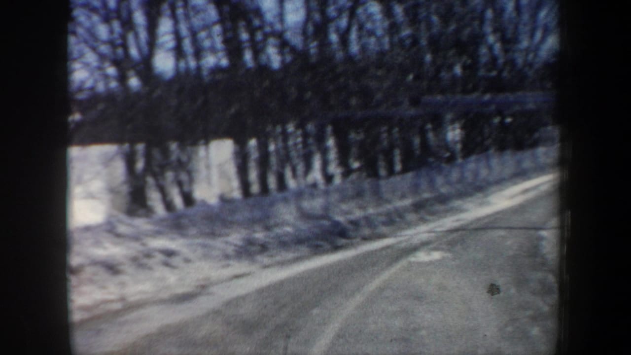 1962 New Hampshire home-movie view from inside a moving car on a snow-lined road with bare winter trees.