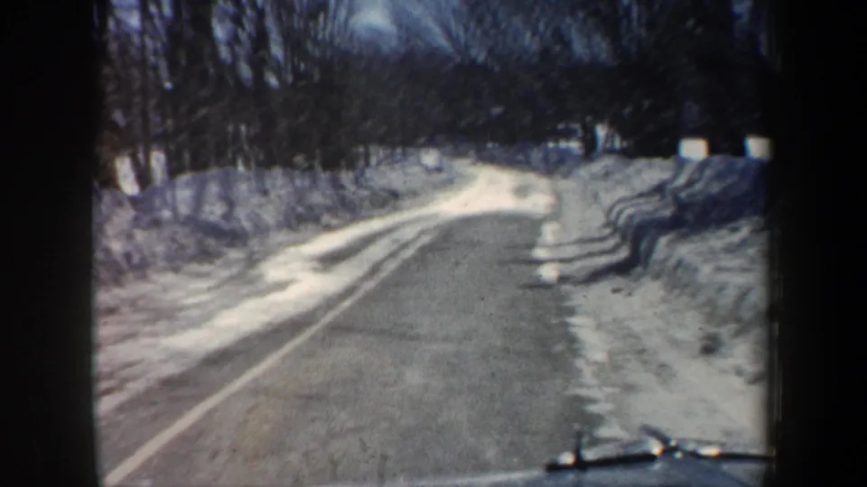 Home-movie travel shot along a narrow New Hampshire winter road with snow piled beside the pavement.