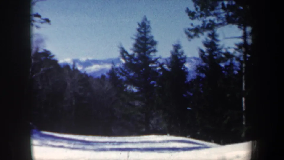 1962 New Hampshire 8mm frame showing snow-covered ground with evergreen trees and dark film-frame edges.