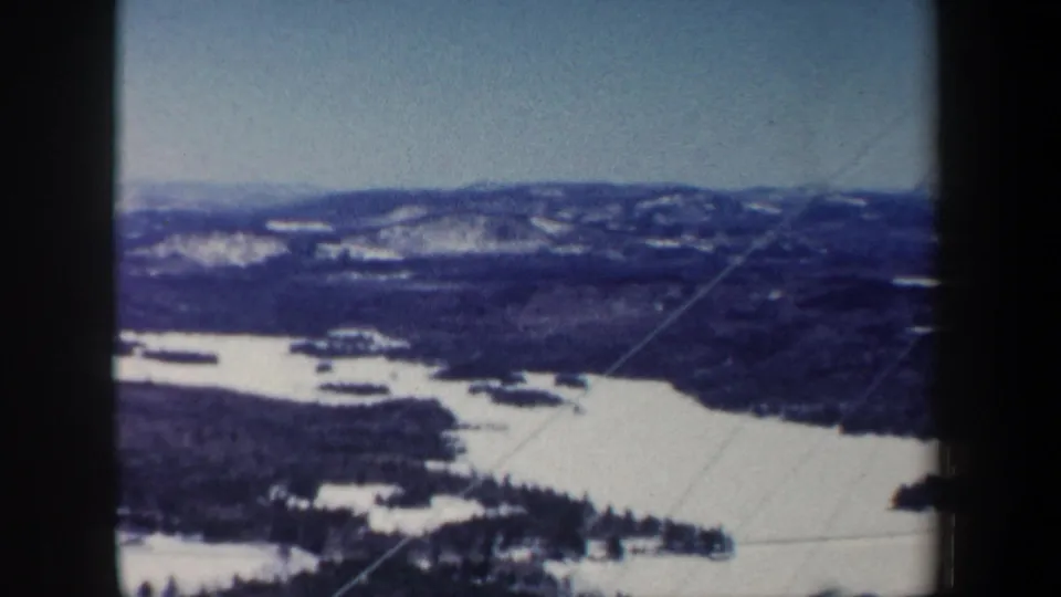 Wide 1962 New Hampshire 8mm view of a snowy valley, frozen water, wooded areas, and low hills beyond.