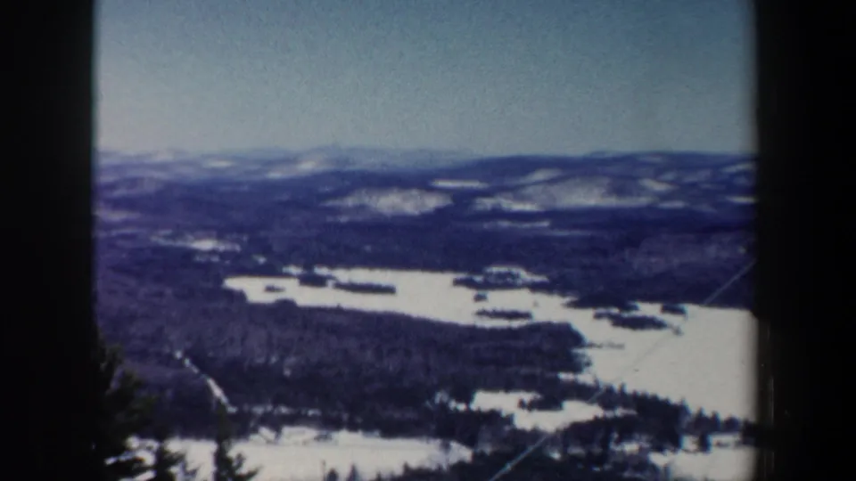 1962 New Hampshire overlook frame with frozen water, snow-covered land, forested hills, and soft blue 8mm color.