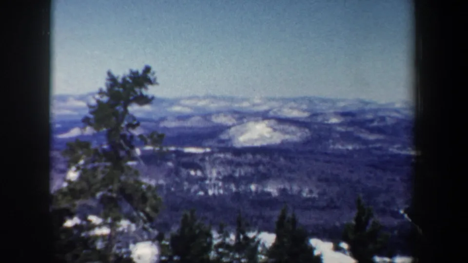 1962 New Hampshire 8mm frame showing evergreen pines against a broad winter mountain view.