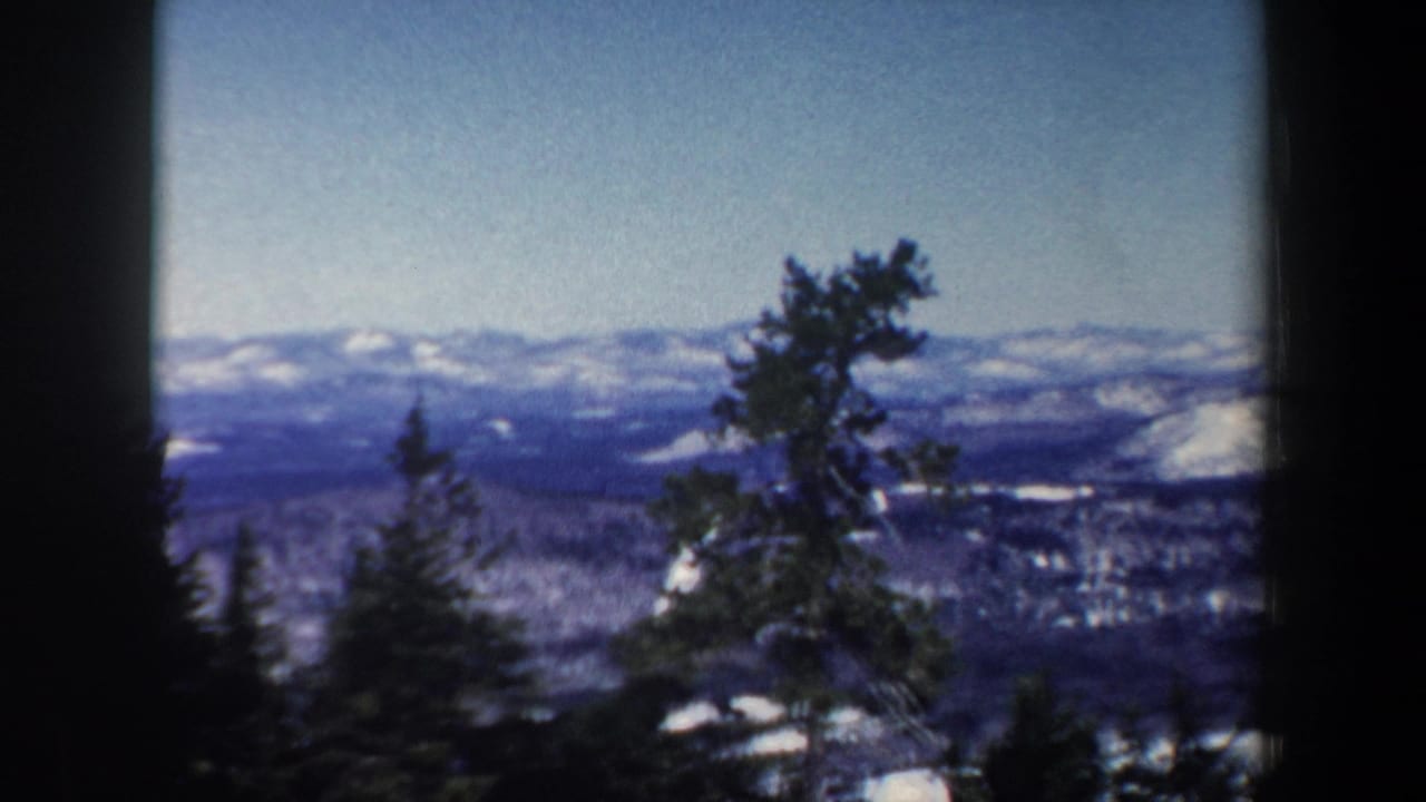 1962 New Hampshire home-movie frame showing dark evergreens in the foreground and snowy mountain ridges in the distance.