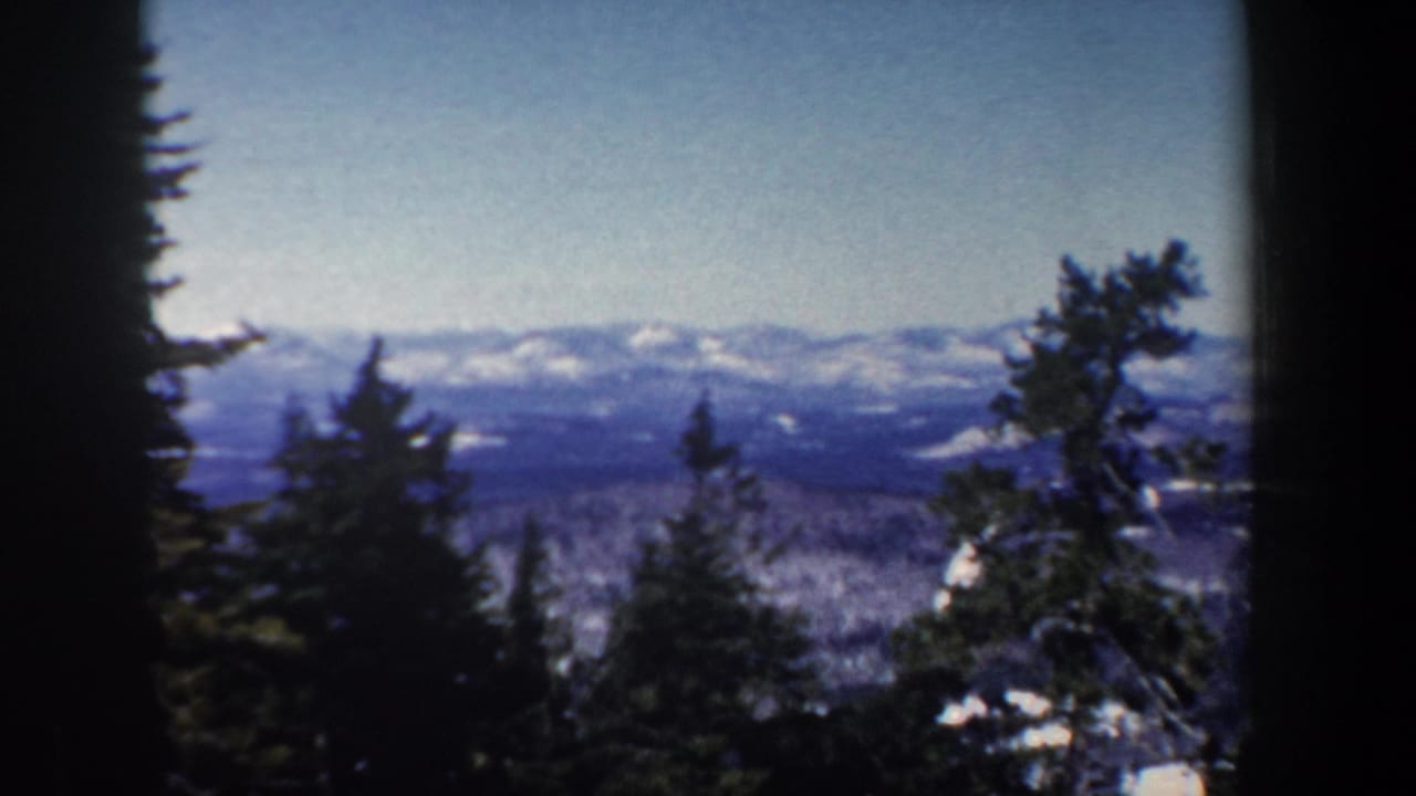 1962 New Hampshire landscape frame with evergreen silhouettes, patchy snow, and distant blue mountain ridges.