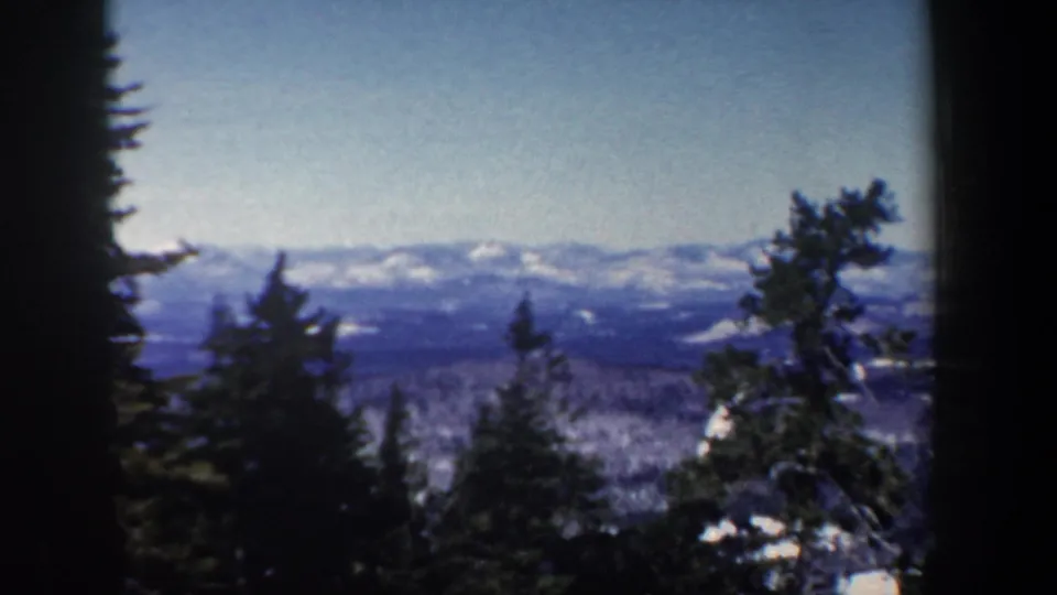 1962 New Hampshire landscape frame with evergreen silhouettes, patchy snow, and distant blue mountain ridges.