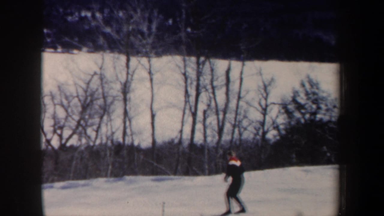 1962 New Hampshire home-movie frame showing a lone skier crossing a snowy slope near leafless woods.