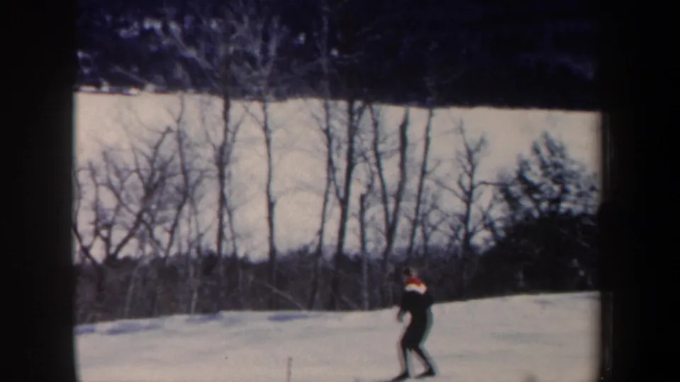 1962 New Hampshire home-movie frame showing a lone skier crossing a snowy slope near leafless woods.