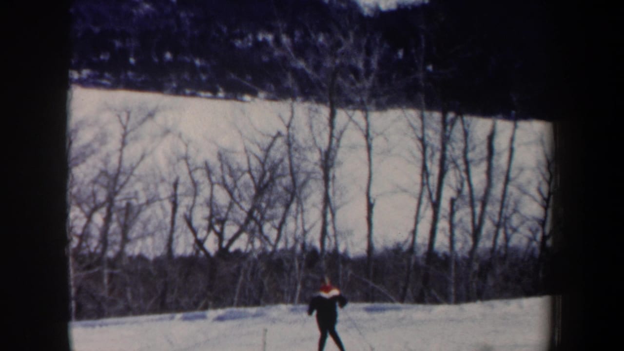 1962 New Hampshire frame with a distant skier gliding across a snow-covered hill bordered by leafless trees.
