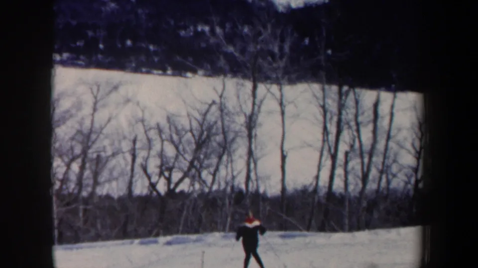 1962 New Hampshire frame with a distant skier gliding across a snow-covered hill bordered by leafless trees.