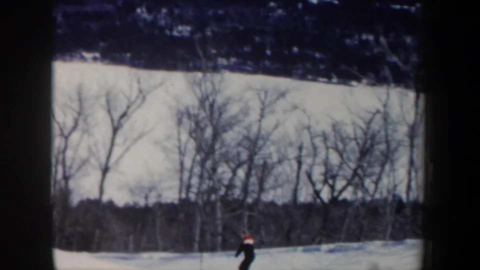 1962 New Hampshire home-movie still showing a lone skier low in frame against a snowy slope and winter woods.