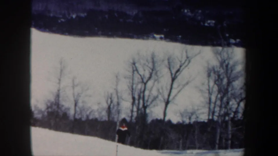 1962 New Hampshire frame showing a small skier near the wooded edge of a snow-covered slope.