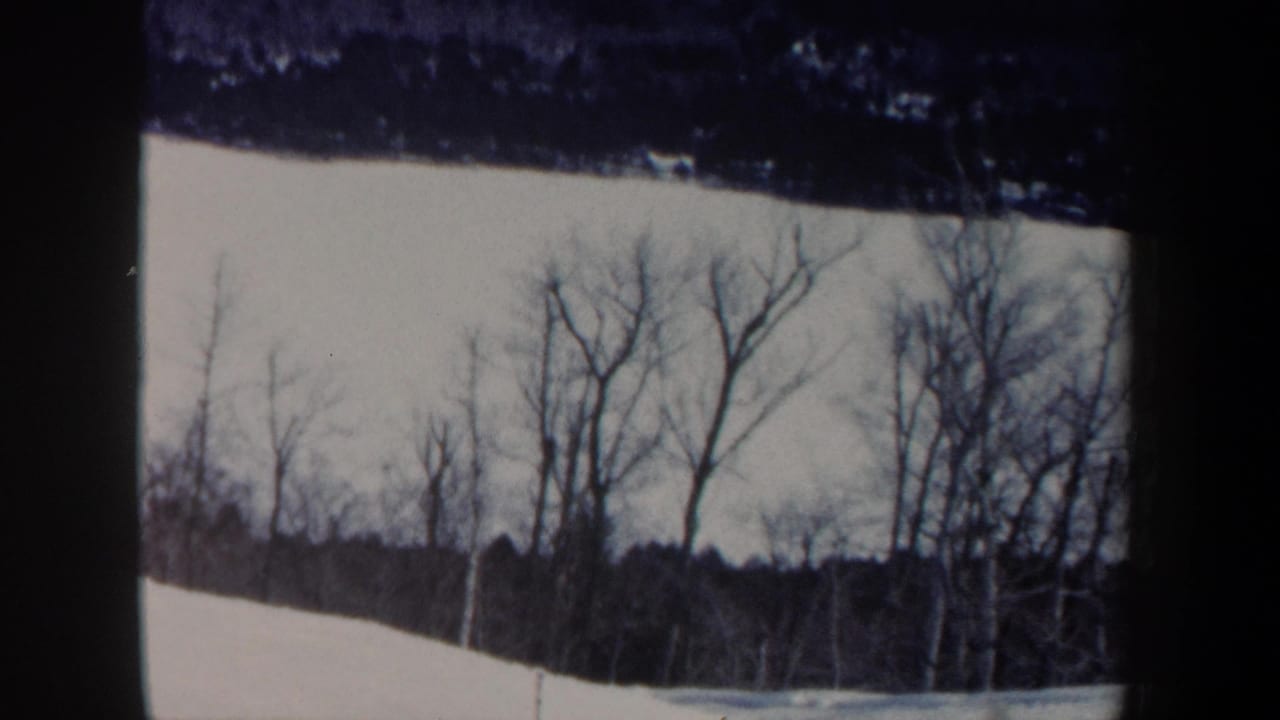 1962 New Hampshire frame with a small skier on a snowy hillside, framed by bare trees and dark 8mm borders.