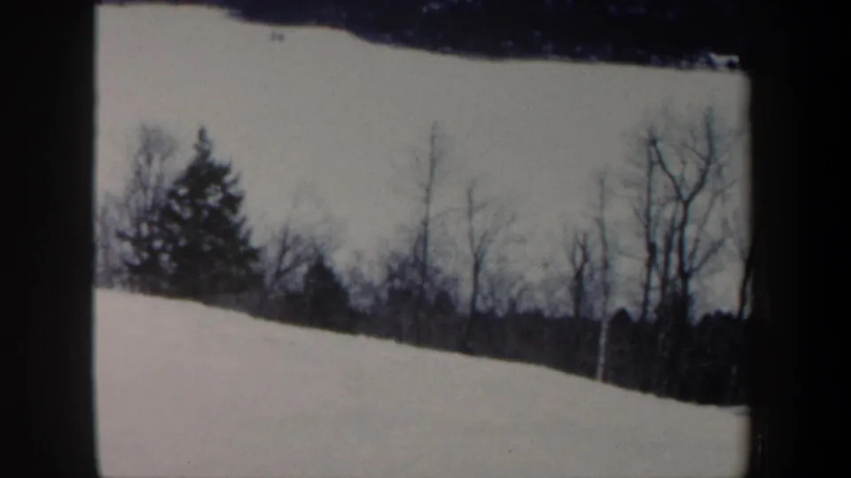 1962 New Hampshire winter frame showing a snowy slope, bare trees, and distant treeline after the skier has moved out of clear view.