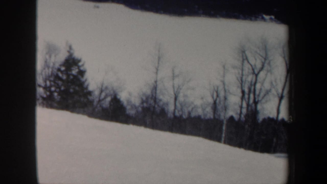1962 New Hampshire 8mm frame showing a snow-covered slope bordered by bare winter trees and dark distant woods.