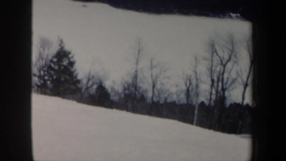 1962 New Hampshire 8mm frame showing a snow-covered slope bordered by bare winter trees and dark distant woods.
