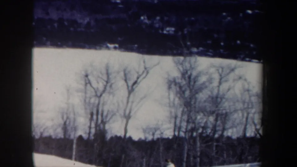 The skier appears near the lower right edge of a snowy New Hampshire slope, partly framed by bare trees in the 1962 home movie.
