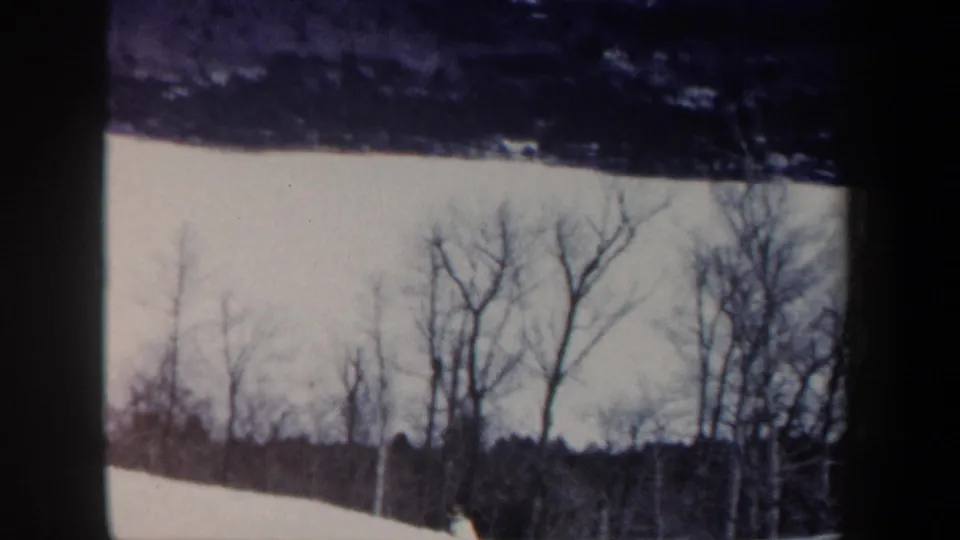 New Hampshire 1962 home-movie frame showing snow, bare winter trees, and a dark forest line at a ski area.