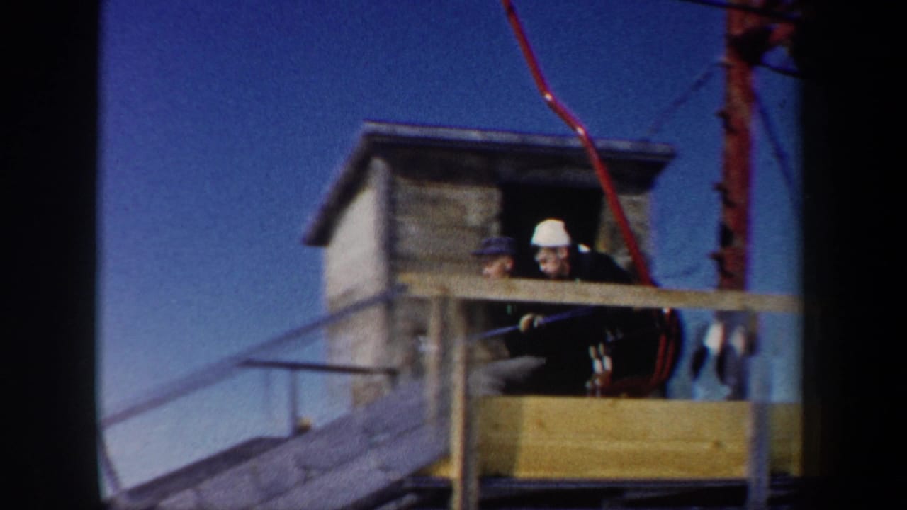 Two workers stand by a wooden ski lift station with a red lift component overhead.