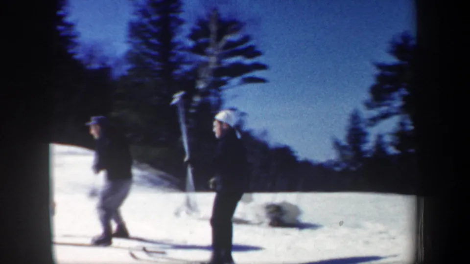 New Hampshire 1962 home-movie frame showing skiers on snow near the edge of a wooded ski slope.