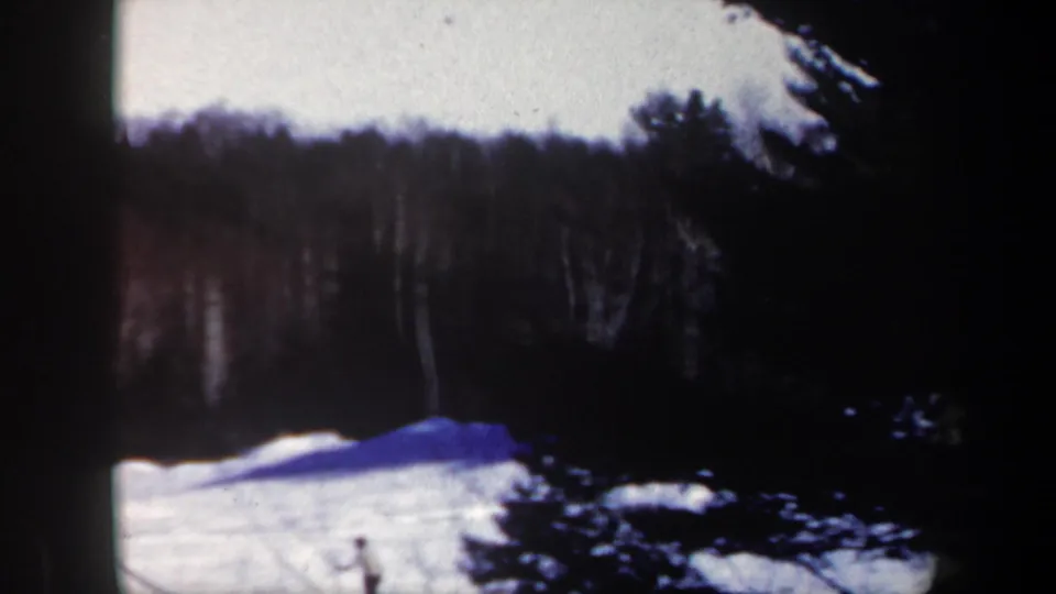 1962 New Hampshire 8mm frame looking across a snow-covered ski slope with evergreens and dense forest beyond.