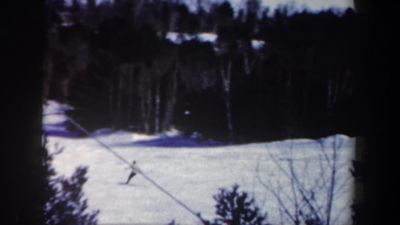 1962 New Hampshire 8mm frame showing a distant skier descending a snowy wooded slope beside a diagonal cable line.