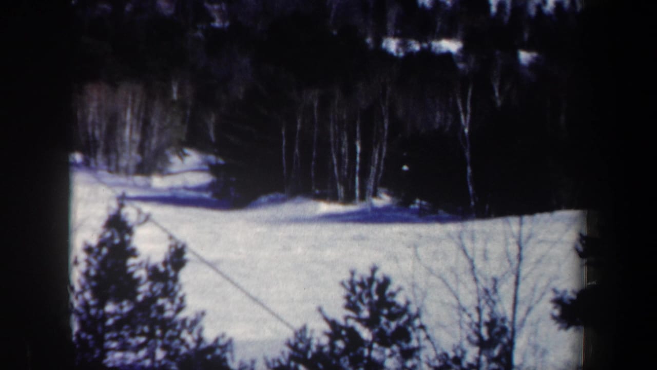 1962 New Hampshire winter home-movie frame with snow, forest, and a diagonal cable line across the slope.