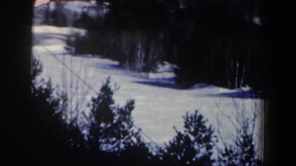 1962 New Hampshire 8mm frame of a wooded ski slope, snowfield, and diagonal cable line in soft focus.