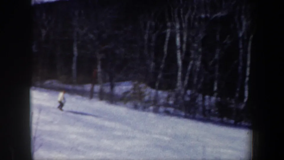 1962 New Hampshire 8mm frame showing a lone skier in a light jacket descending a snowy forest slope.