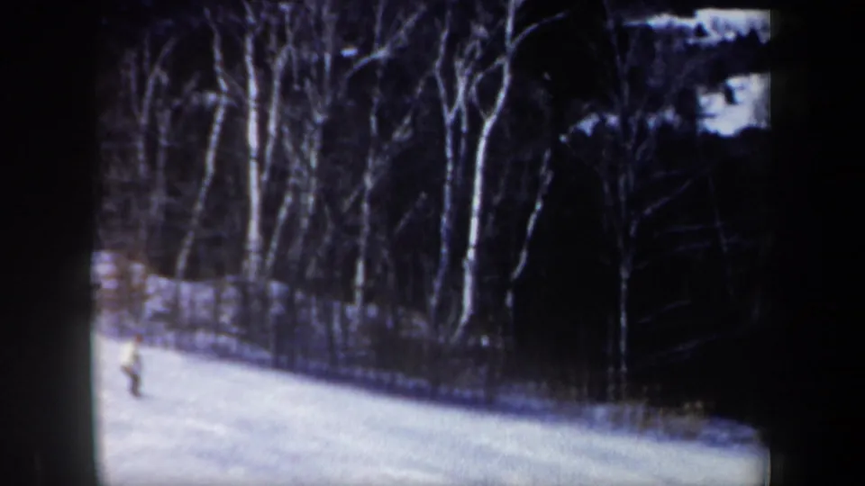 1962 New Hampshire home-movie frame showing a distant skier on a bright snowy slope near bare winter trees.
