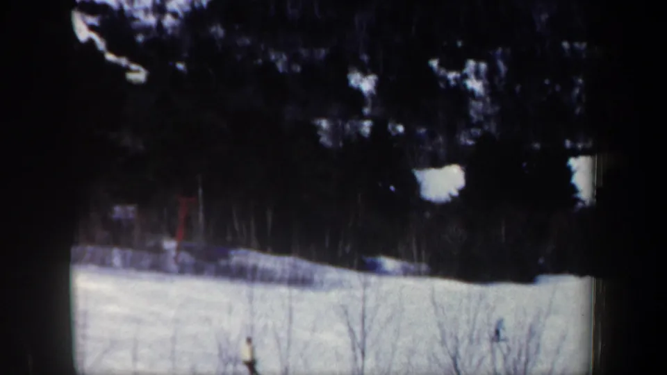 Two distant skiers appear on a sunny New Hampshire snow slope with dark trees in the background.