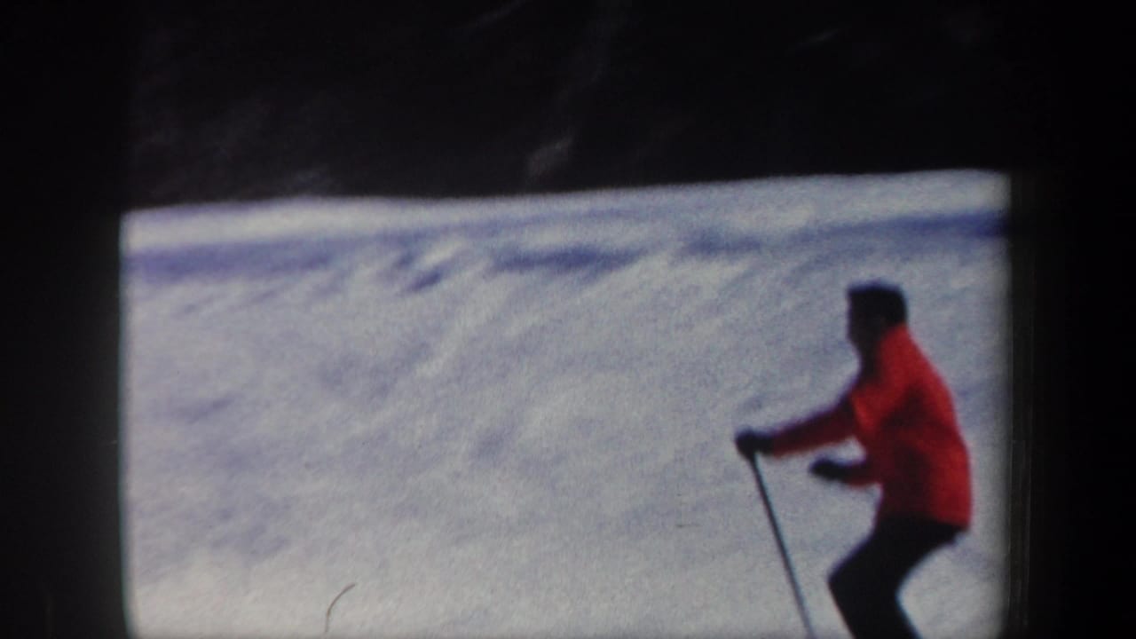 Skier in a red jacket crosses a snowy slope near dark trees.