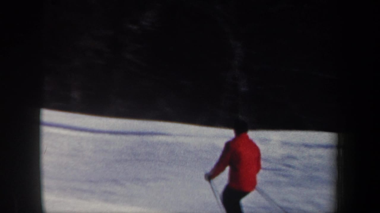 1962 New Hampshire home-movie frame with a red-jacketed skier seen from behind on a snowy slope near evergreens.