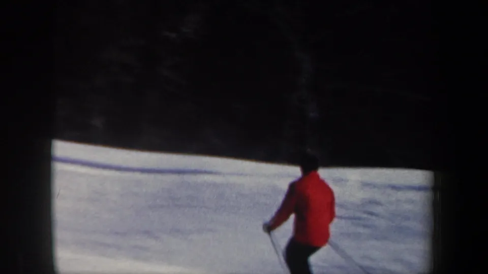 1962 New Hampshire home-movie frame with a red-jacketed skier seen from behind on a snowy slope near evergreens.