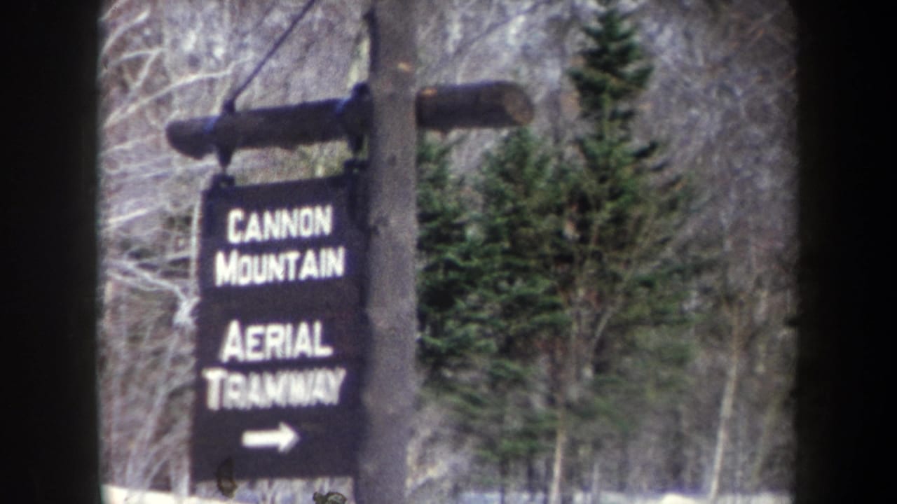 1962 8mm frame showing a Cannon Mountain Aerial Tramway sign with white lettering and arrow in a snowy forest setting.