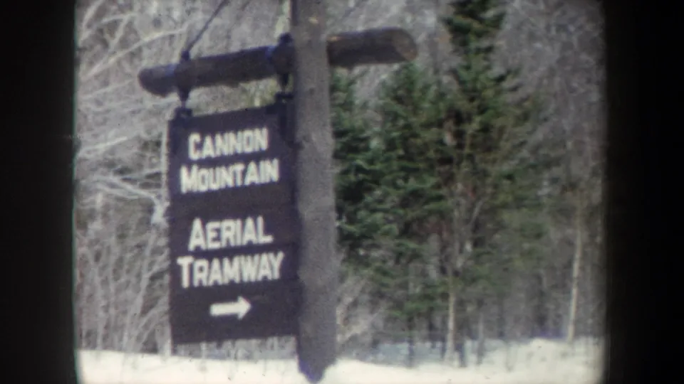 A soft 8mm frame centers the Cannon Mountain Aerial Tramway sign, with snowy ground and winter forest visible behind it.