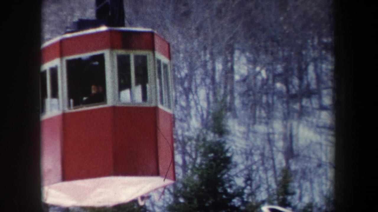 1962 New York 8mm frame showing a red cable car cabin with white-trimmed windows moving past bare trees.