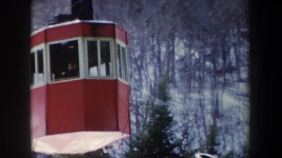 1962 New York 8mm frame showing a red cable car cabin with white-trimmed windows moving past bare trees.