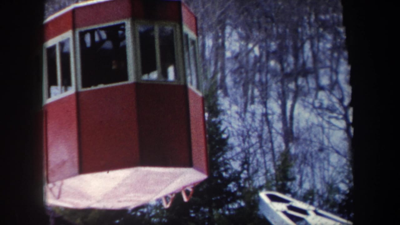 Red cable car cabin suspended near a wooded slope.
