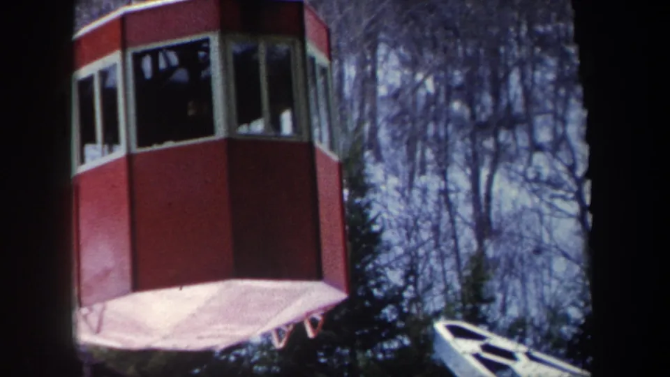 Red octagonal cable car cabin with passengers visible through the windows against bare trees in New York archival footage.